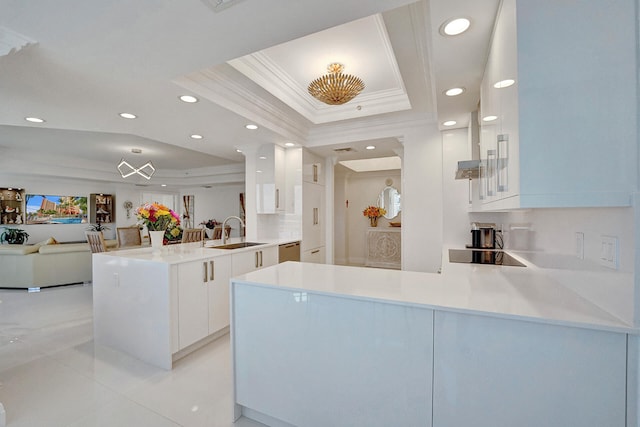 kitchen with ornamental molding, kitchen peninsula, white cabinets, and a raised ceiling