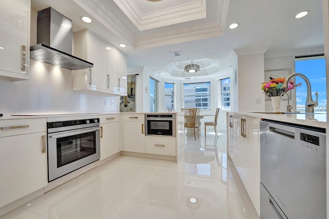 kitchen featuring appliances with stainless steel finishes, wall chimney exhaust hood, white cabinetry, and a healthy amount of sunlight