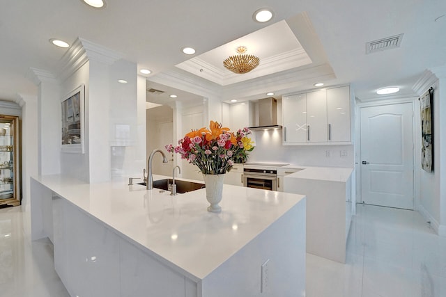 kitchen featuring oven, wall chimney exhaust hood, kitchen peninsula, a tray ceiling, and white cabinets