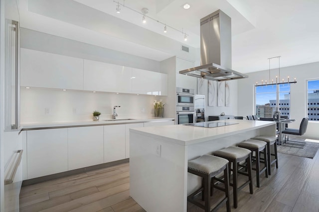 kitchen featuring island exhaust hood, white cabinetry, a center island, and light hardwood / wood-style floors