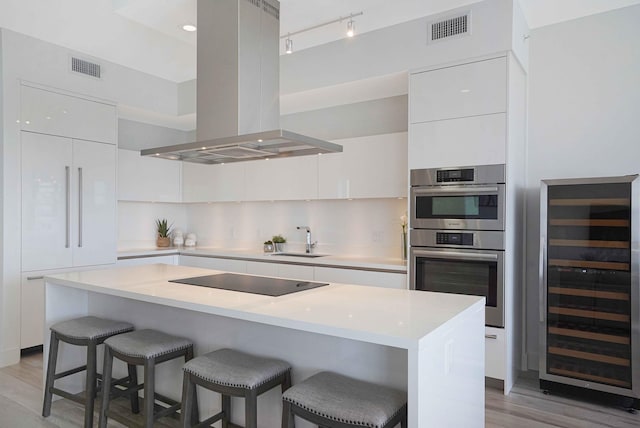 kitchen with white cabinets, wine cooler, island range hood, black electric cooktop, and light hardwood / wood-style floors