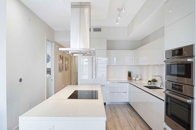 kitchen featuring black electric stovetop, island exhaust hood, light hardwood / wood-style flooring, and white cabinetry