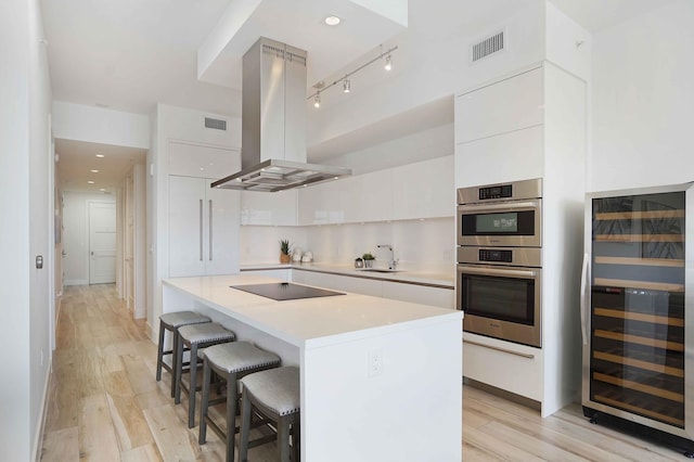 kitchen with light wood-type flooring, white cabinets, stainless steel double oven, beverage cooler, and island exhaust hood