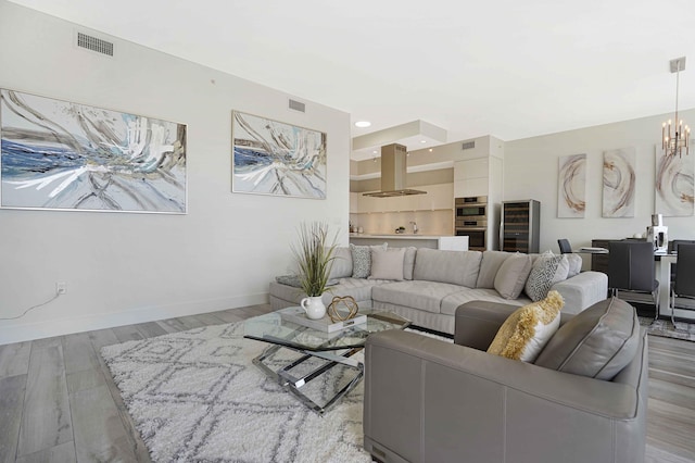 living room with an inviting chandelier, beverage cooler, and light wood-type flooring