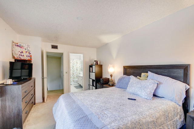 bedroom featuring a textured ceiling, light colored carpet, and ensuite bathroom