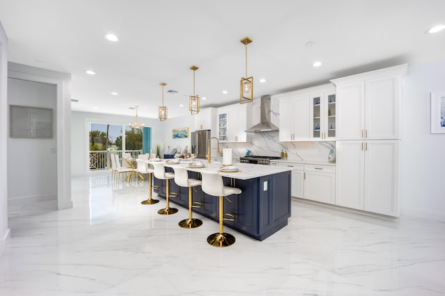 kitchen with white cabinets, a center island with sink, decorative light fixtures, light tile patterned flooring, and wall chimney exhaust hood