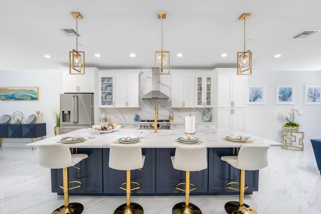 kitchen featuring light tile patterned floors, hanging light fixtures, wall chimney exhaust hood, high end refrigerator, and a spacious island