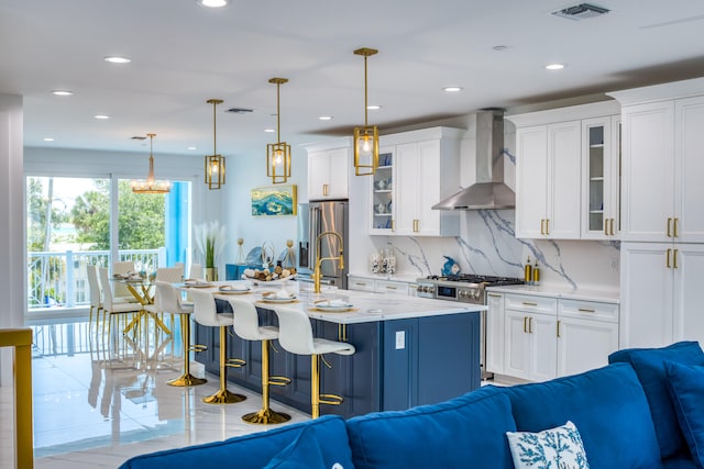 kitchen featuring appliances with stainless steel finishes, white cabinetry, decorative light fixtures, and wall chimney range hood