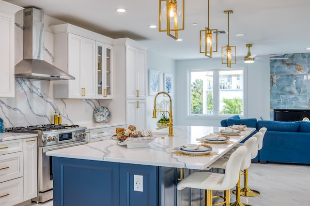 kitchen featuring high end stainless steel range oven, wall chimney range hood, pendant lighting, light tile patterned floors, and an island with sink