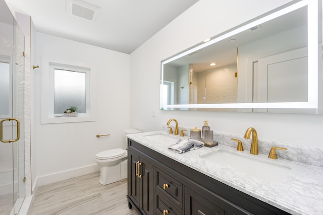 bathroom featuring a shower with door, double vanity, and toilet