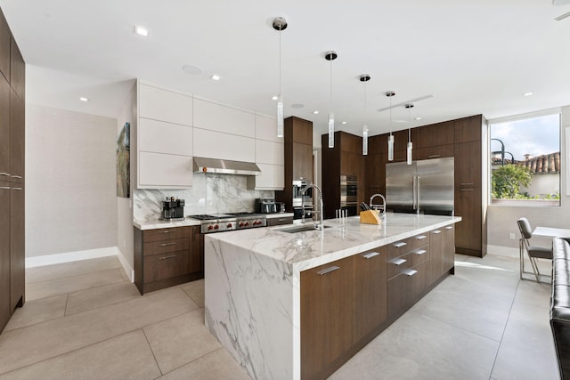 kitchen with pendant lighting, a center island with sink, sink, white cabinets, and light stone counters