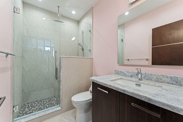 bathroom featuring tile walls, toilet, a shower with door, tile flooring, and vanity