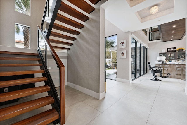 stairway featuring a notable chandelier, light tile flooring, and a towering ceiling