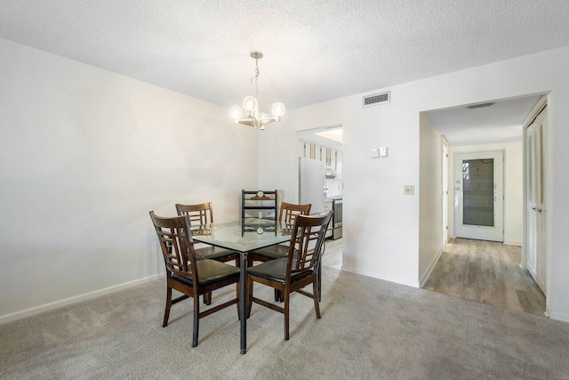 dining area featuring light colored carpet, a notable chandelier, and a textured ceiling