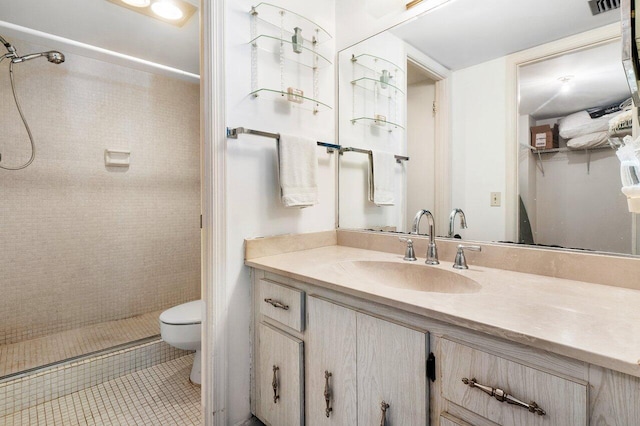 bathroom featuring toilet, a tile shower, vanity with extensive cabinet space, and tile flooring