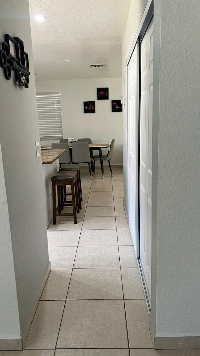 hallway with a textured ceiling and light tile floors