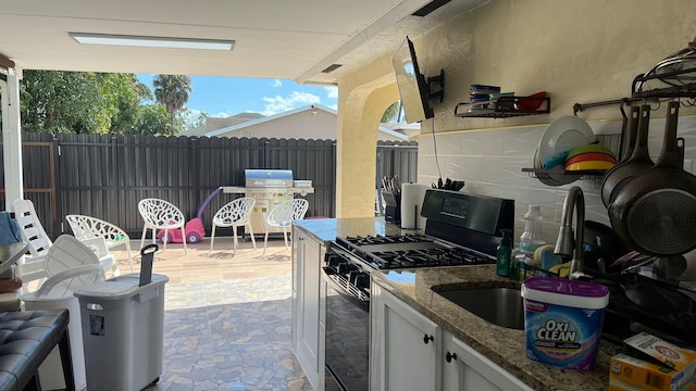 exterior space with light tile floors, light stone countertops, white cabinetry, and gas range oven