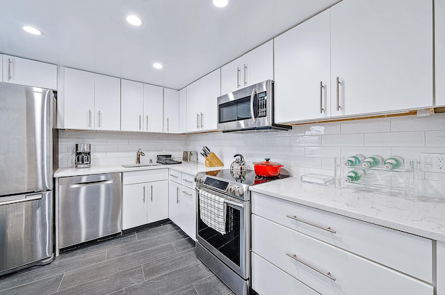 kitchen featuring stainless steel appliances, light stone countertops, white cabinetry, backsplash, and sink