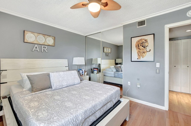 bedroom featuring baseboards, visible vents, light wood-style flooring, a textured ceiling, and crown molding