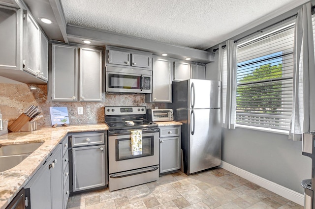 kitchen featuring baseboards, appliances with stainless steel finishes, gray cabinets, and decorative backsplash