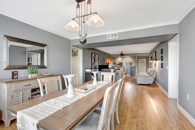 dining room featuring crown molding, visible vents, light wood-style flooring, a textured ceiling, and baseboards