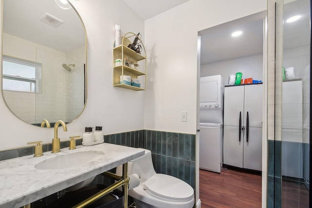 bathroom featuring toilet, hardwood / wood-style flooring, vanity, tile walls, and stacked washer and clothes dryer