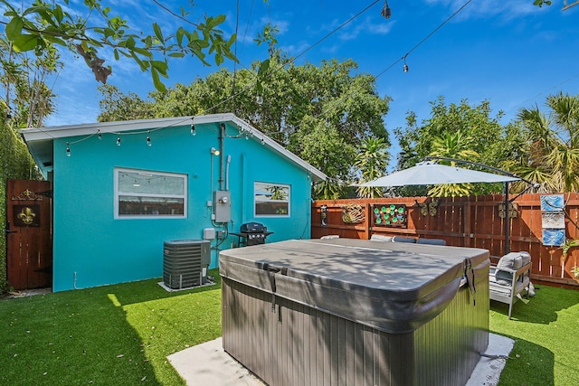 back of property featuring a hot tub, central air condition unit, and a yard