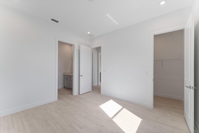 unfurnished bedroom featuring ensuite bathroom, a spacious closet, a closet, and light wood-type flooring