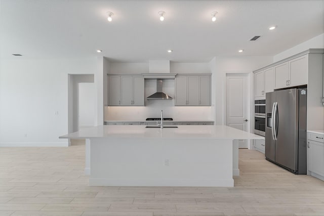 kitchen featuring a kitchen island with sink, wall chimney range hood, gray cabinets, and stainless steel appliances