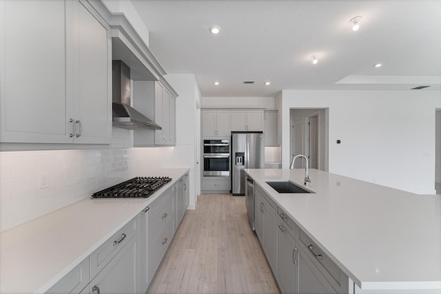 kitchen with tasteful backsplash, sink, a large island with sink, stainless steel appliances, and wall chimney exhaust hood