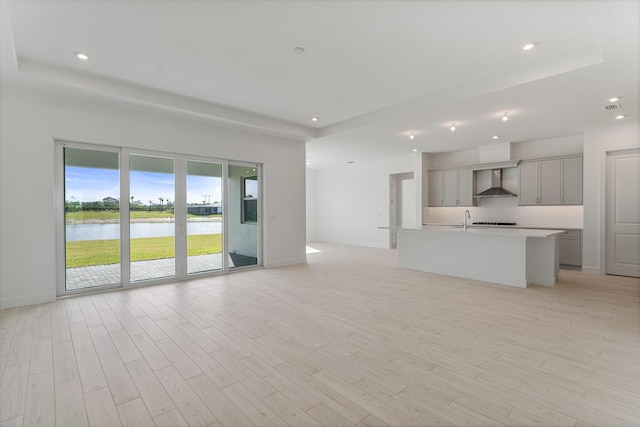 unfurnished living room featuring light wood-type flooring, a raised ceiling, and a water view