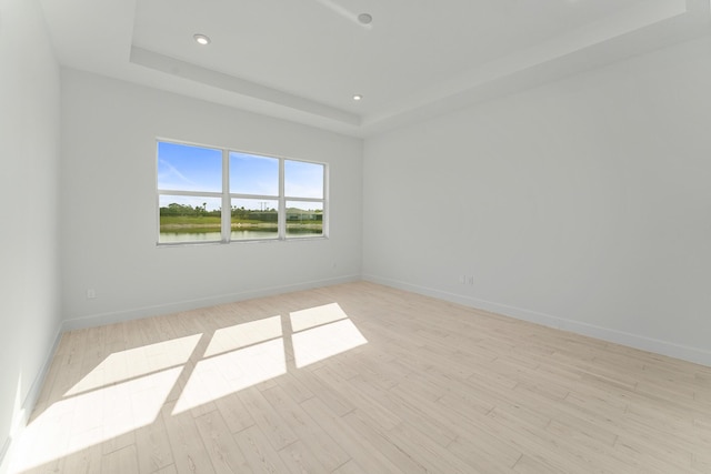 spare room with a water view, a raised ceiling, and light hardwood / wood-style floors