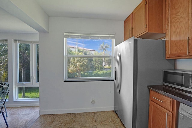 kitchen featuring a wealth of natural light, dark stone countertops, light tile patterned floors, and stainless steel appliances