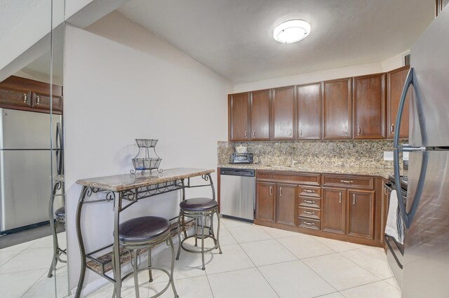 kitchen with light tile patterned floors, backsplash, light stone counters, stainless steel appliances, and sink