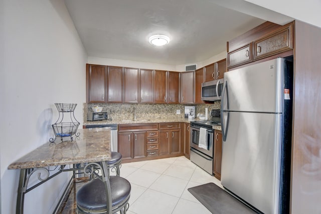 kitchen featuring light tile patterned flooring, backsplash, light stone counters, stainless steel appliances, and sink