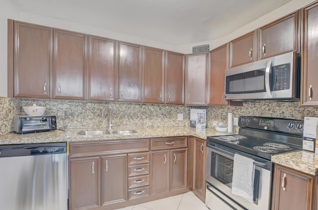 kitchen featuring appliances with stainless steel finishes, a sink, light stone countertops, and decorative backsplash