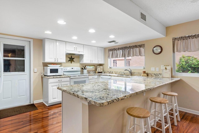 kitchen with white cabinets, dark wood-type flooring, white appliances, and kitchen peninsula