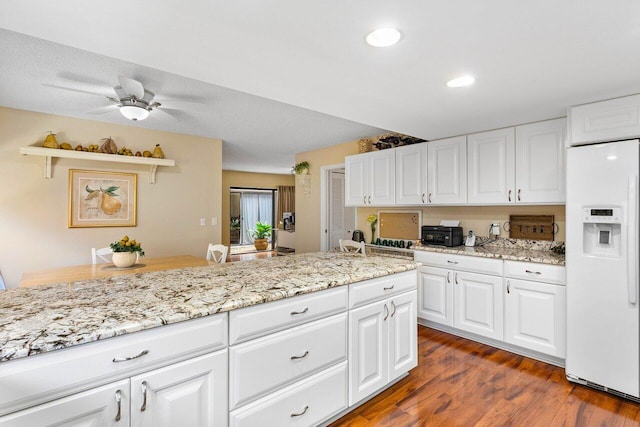 kitchen featuring light stone countertops, ceiling fan, white cabinets, dark wood-type flooring, and white refrigerator with ice dispenser