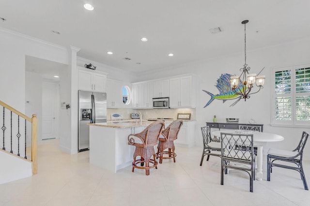 kitchen featuring stainless steel appliances, crown molding, a center island with sink, a notable chandelier, and white cabinets