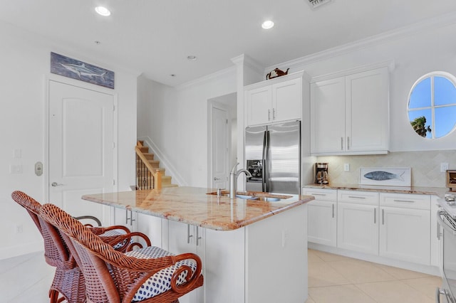 kitchen featuring light stone countertops, stainless steel refrigerator with ice dispenser, sink, white cabinets, and an island with sink