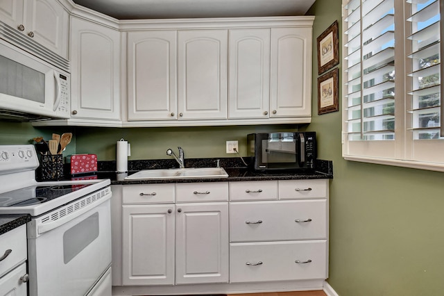 kitchen featuring dark stone counters, white appliances, white cabinetry, and sink