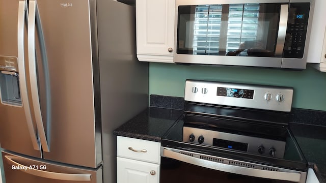 kitchen featuring stainless steel appliances, dark stone countertops, and white cabinetry