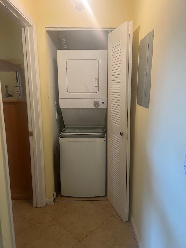 clothes washing area featuring light tile flooring and stacked washing maching and dryer