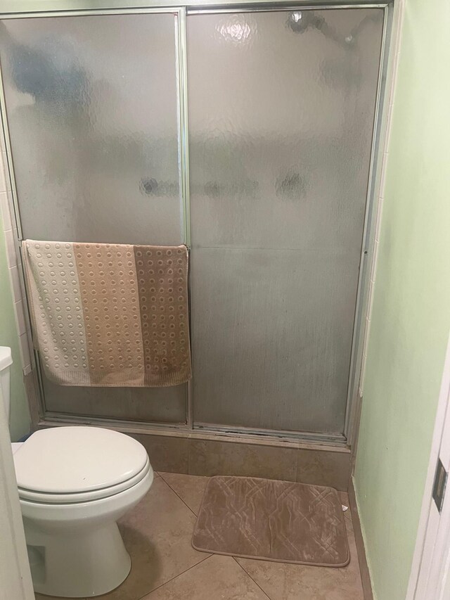 bathroom with toilet, tile floors, and a shower with shower door