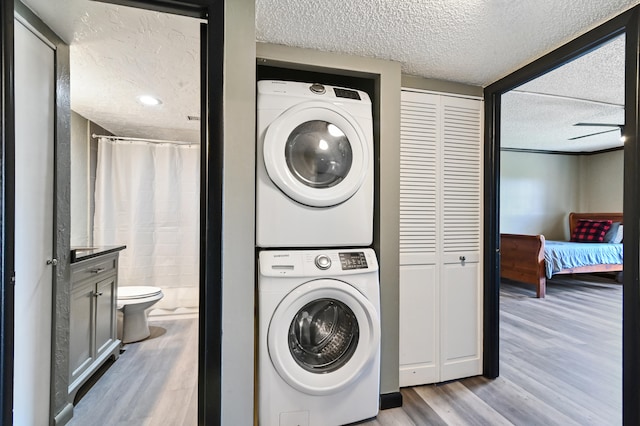 laundry room with a textured ceiling, stacked washer and clothes dryer, ceiling fan, and light wood-type flooring