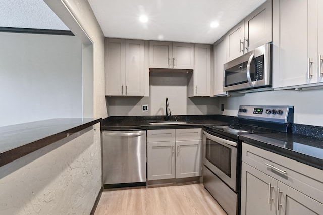 kitchen with stainless steel appliances, dark stone counters, gray cabinets, light hardwood / wood-style flooring, and sink