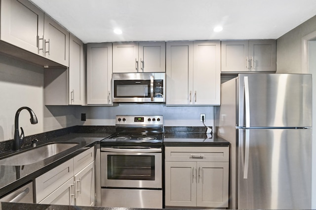 kitchen featuring dark stone countertops, gray cabinets, appliances with stainless steel finishes, and sink