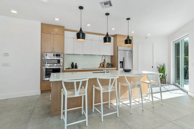 kitchen with white cabinets, an island with sink, decorative light fixtures, and stainless steel appliances