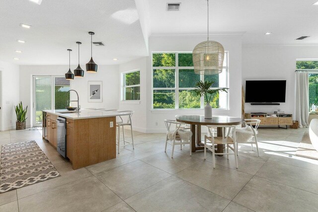 kitchen with pendant lighting, a kitchen island with sink, crown molding, sink, and dishwasher