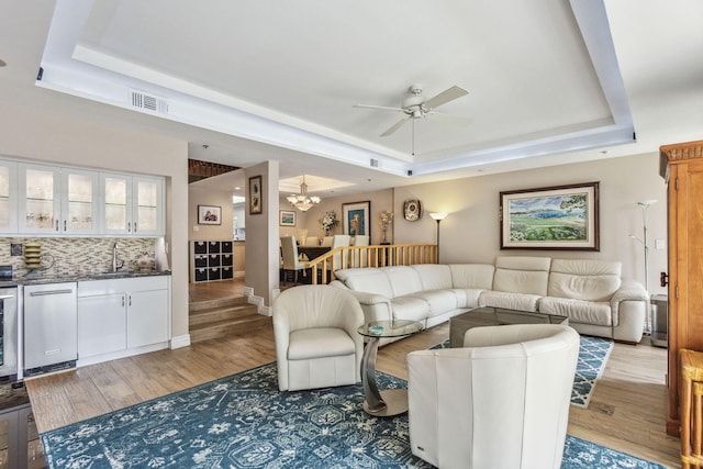 living room featuring sink, ceiling fan with notable chandelier, a tray ceiling, and wood-type flooring